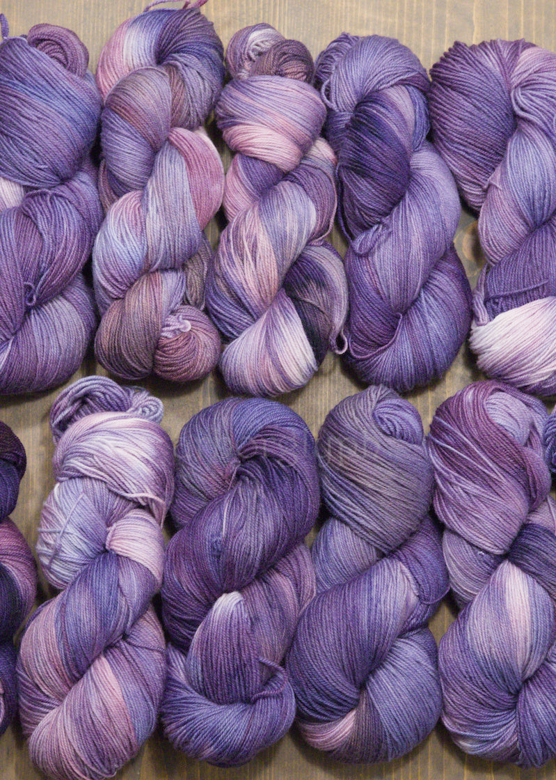 Collection of hand dyed purple and pink Merino yarn skeins on a wooden surface