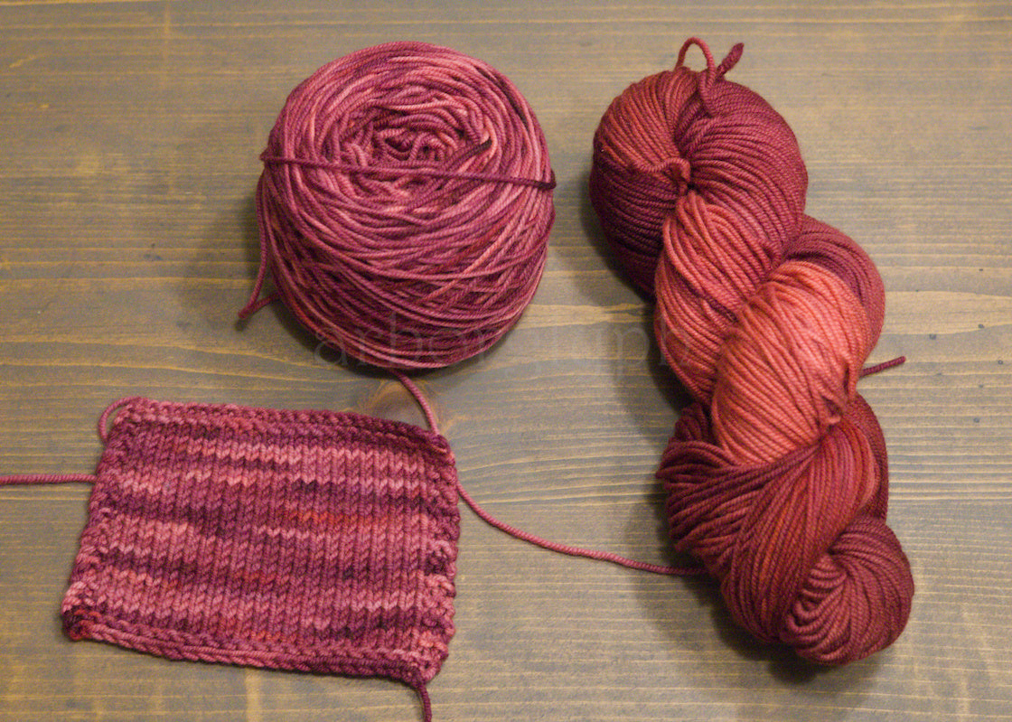 Two skeins of red yarn and a knitted swatch on a wooden surface