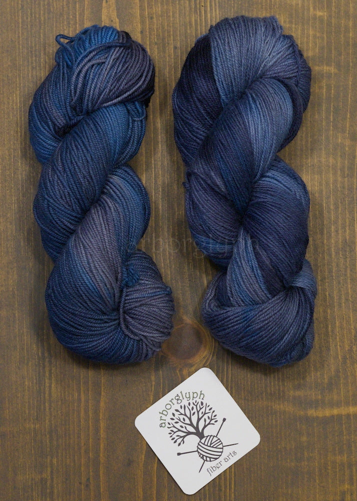 Two skeins of blue yarn on a wooden surface with a brand label.