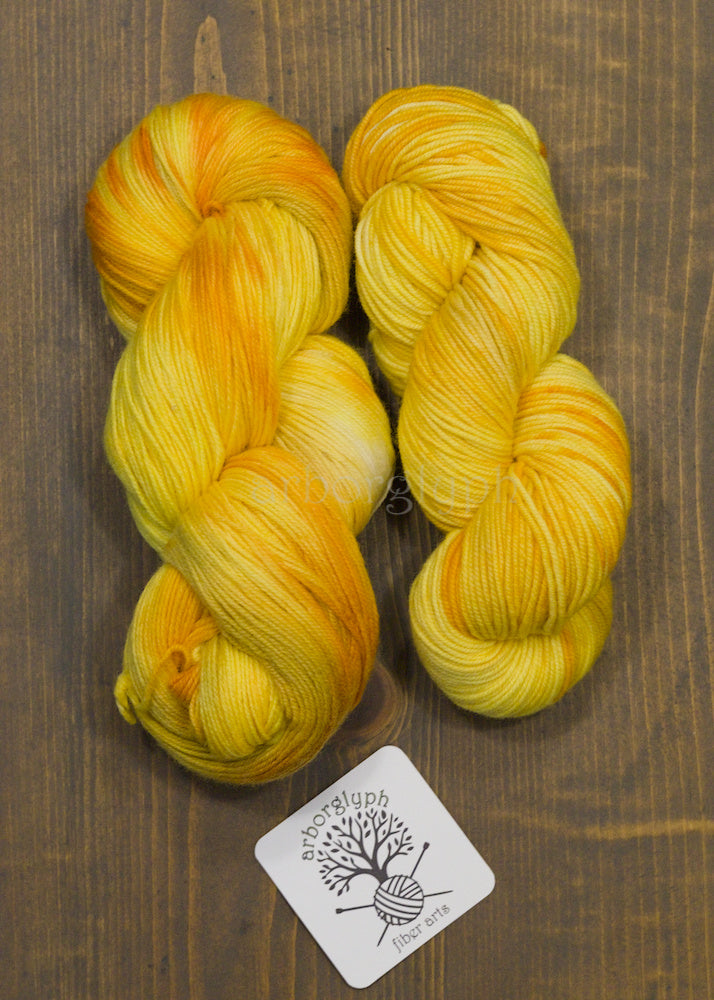 Two skeins of yellow yarn on a wooden surface with a brand label.