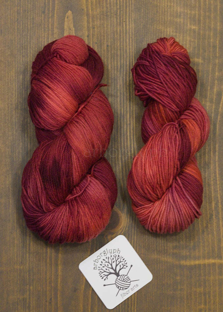 Two skeins of red yarn on a wooden surface with a brand label.