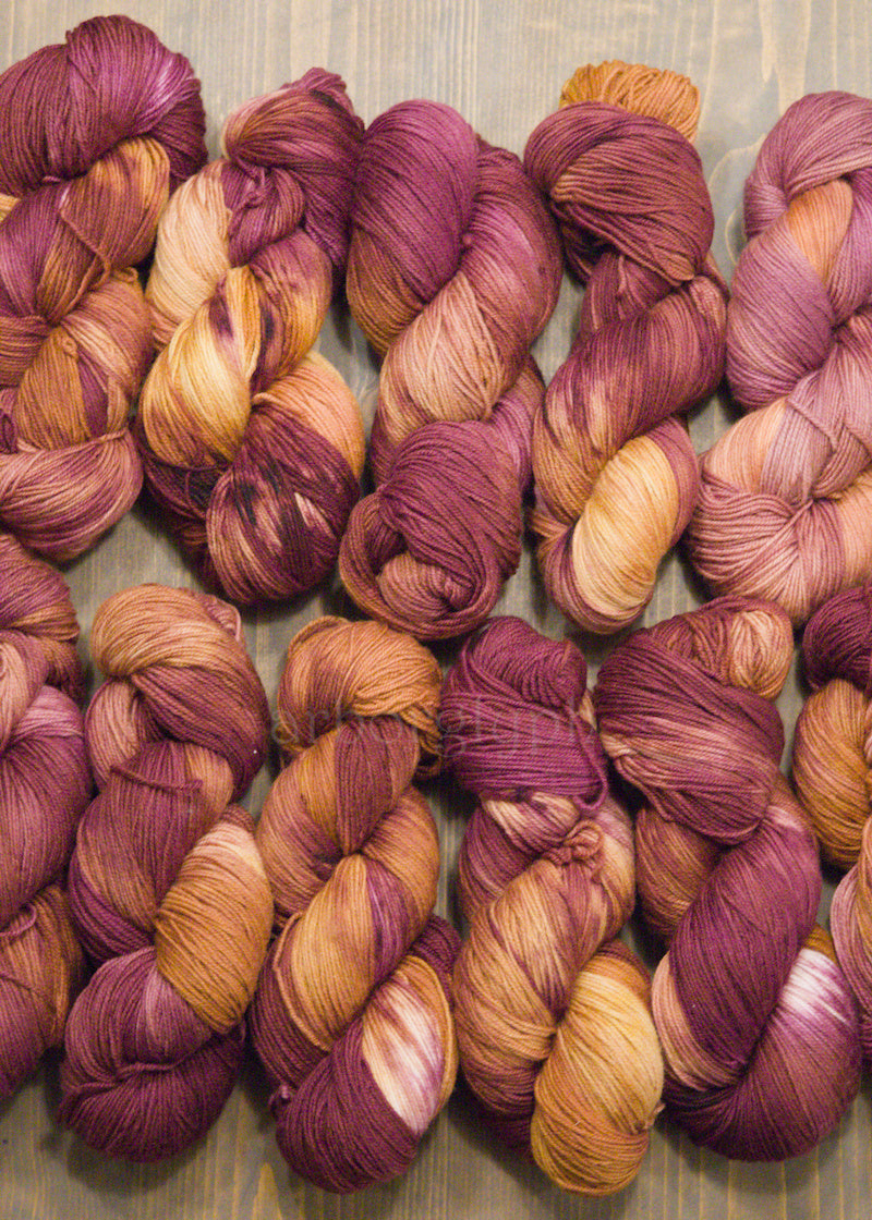 Skeins of hand dyed burgundy and orange Merino yarn on a wooden surface