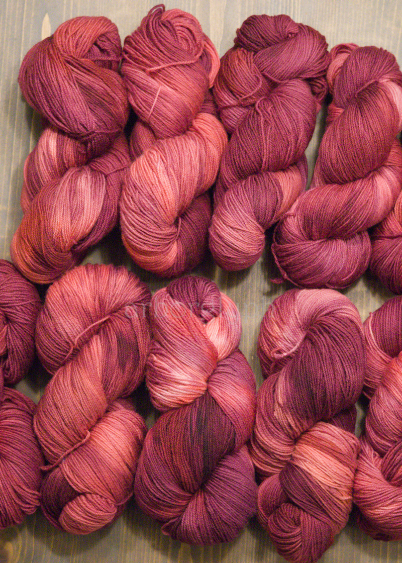 Collection of hand dyed pink and red Merino yarn skeins on a wooden surface