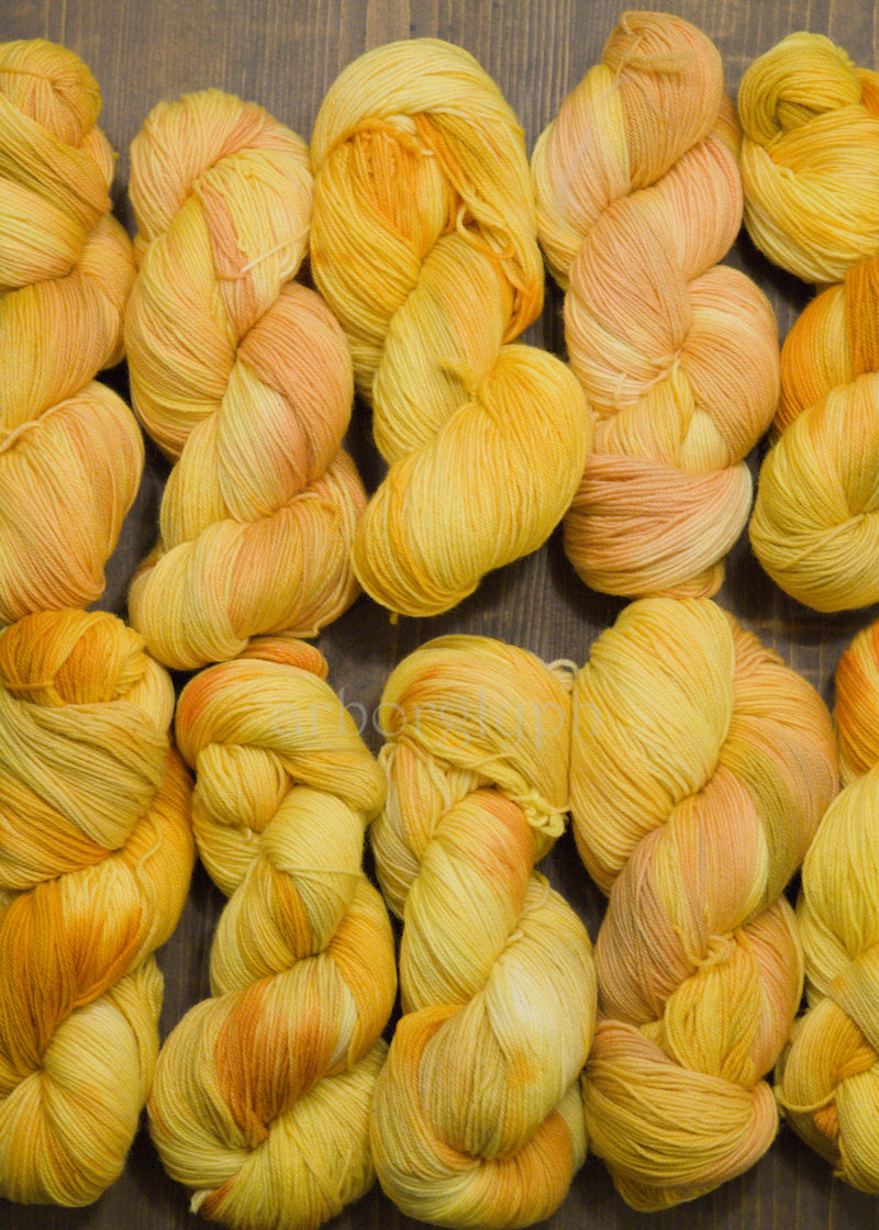 Collection of yellow and orange hand dyed merino yarn skeins on a wooden surface