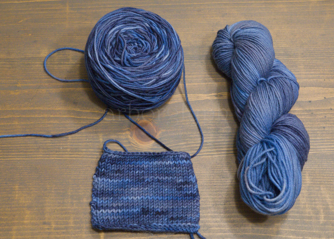 Two skeins of blue yarn and a knitted sample on a wooden surface