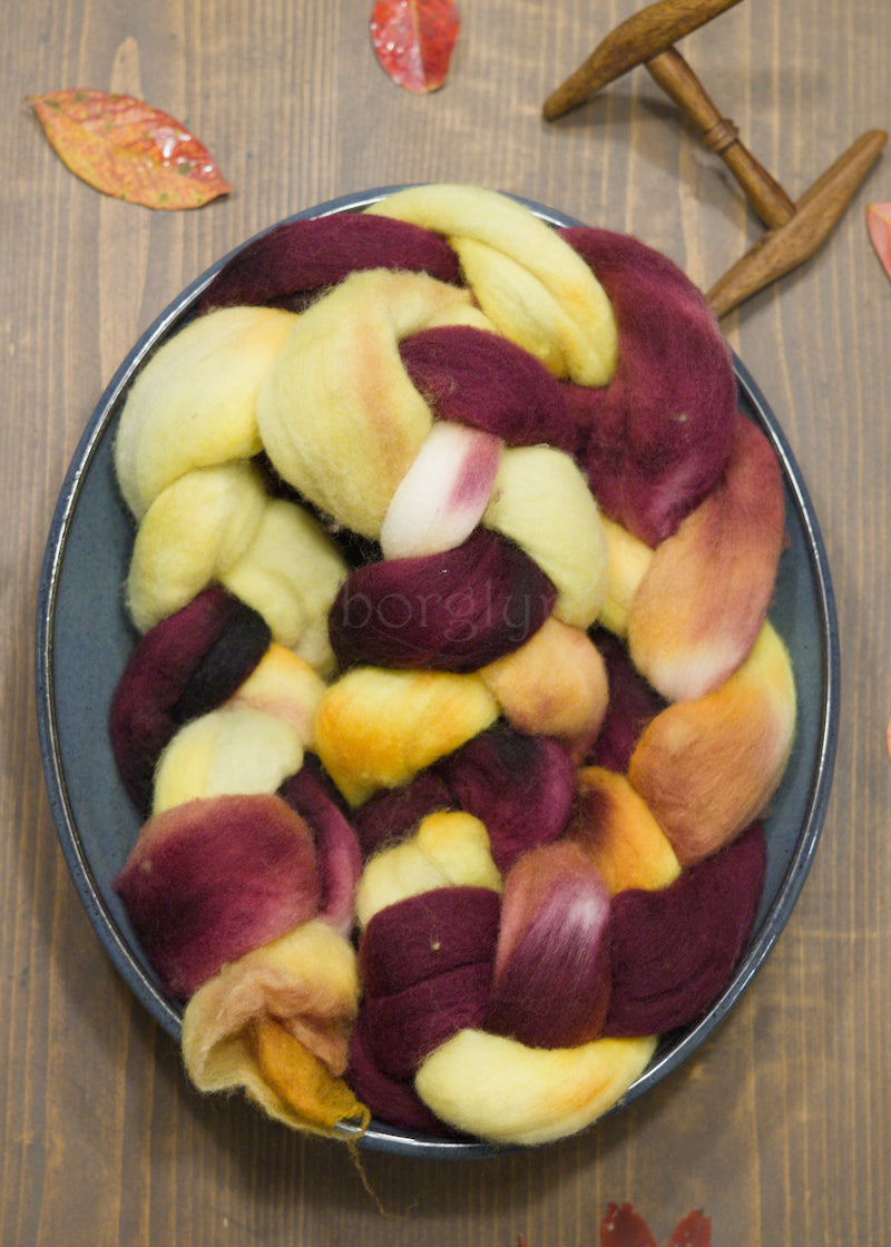 Burgundy, yellow and orange combed Merino top on a wooden surface.