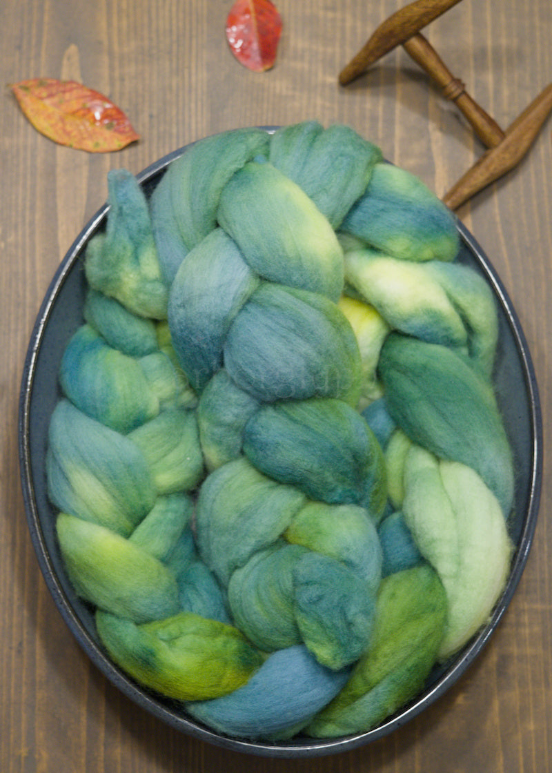 Blue and green combed top in a bowl on a wooden surface