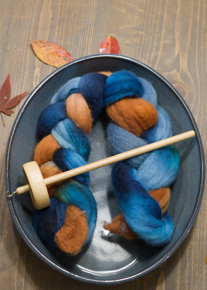 Spindle with blue and orange combed wool top on a wooden surface
