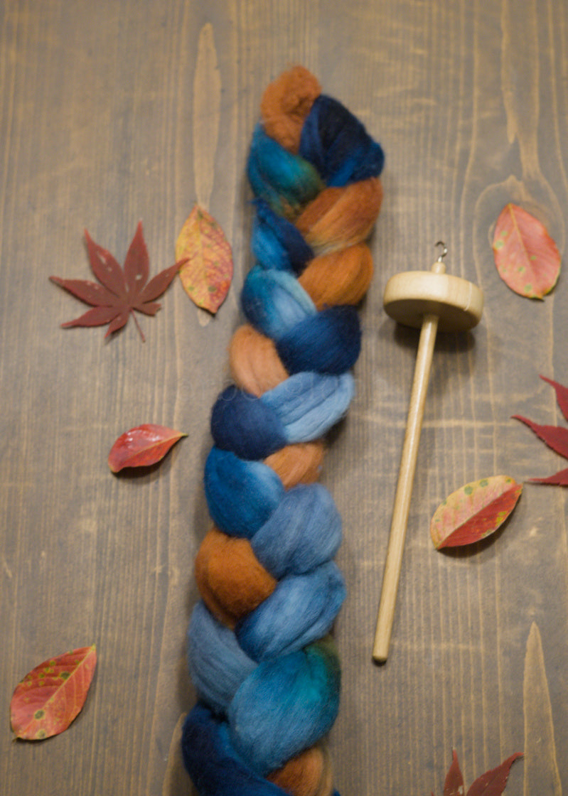 Combed wool top with a spindle on a wooden surface with autumn leaves.