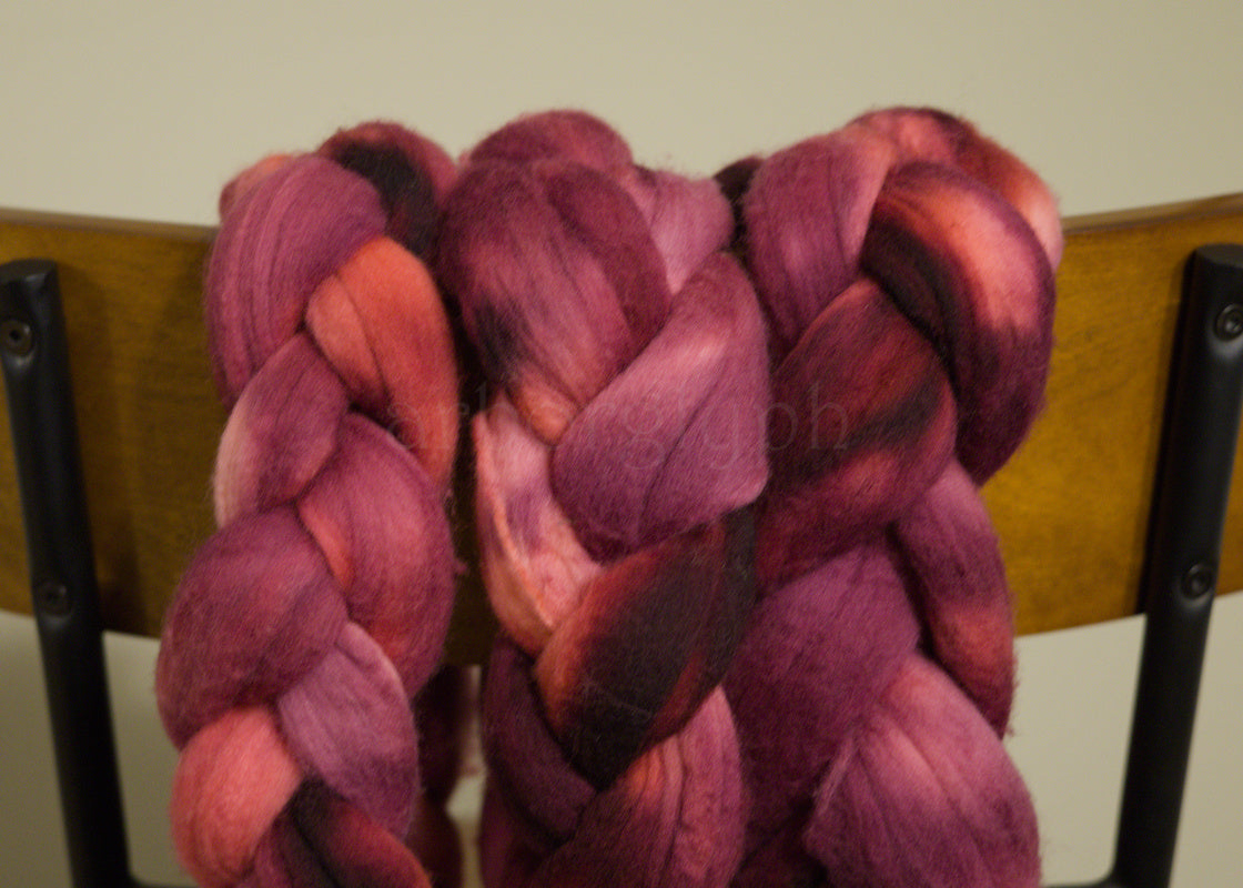Braided combed Merino top of pink and red yarn on a chair