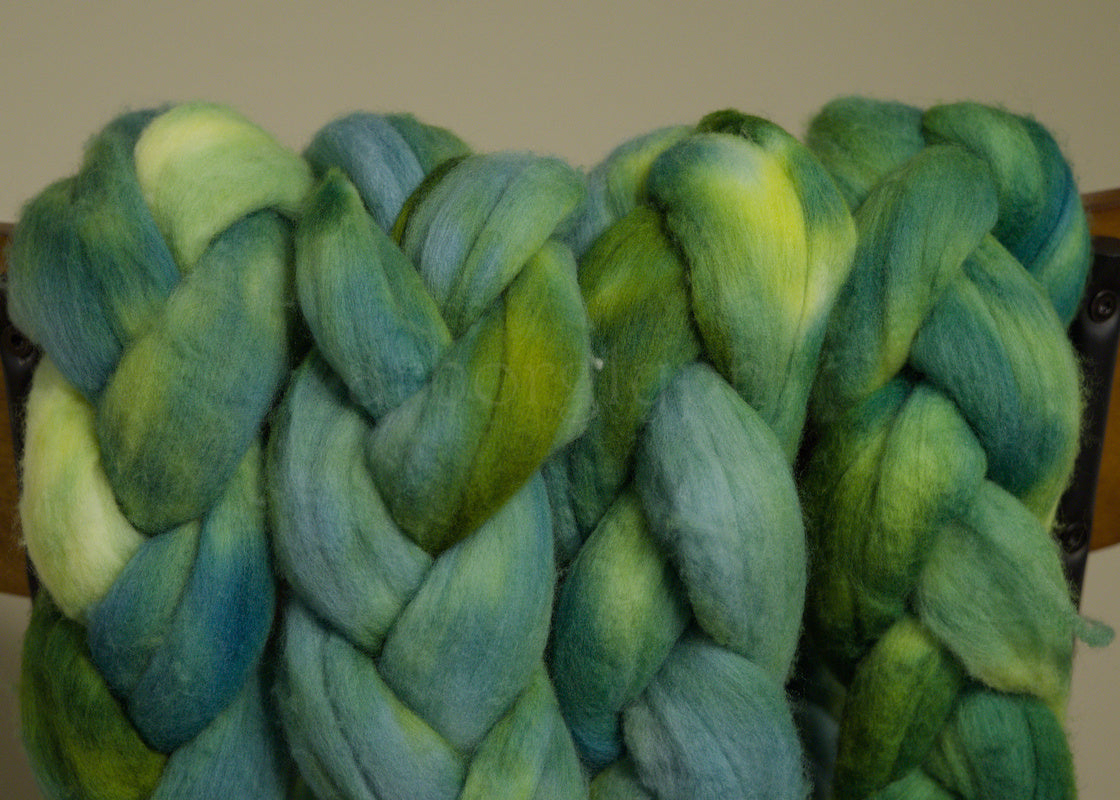Braided Merino combed top of green and blue yarn on a wooden surface