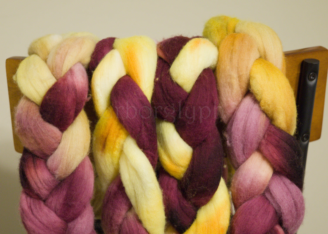 Braided Merino wool top with burgundy, yellow, and pink colors on a wooden stand.