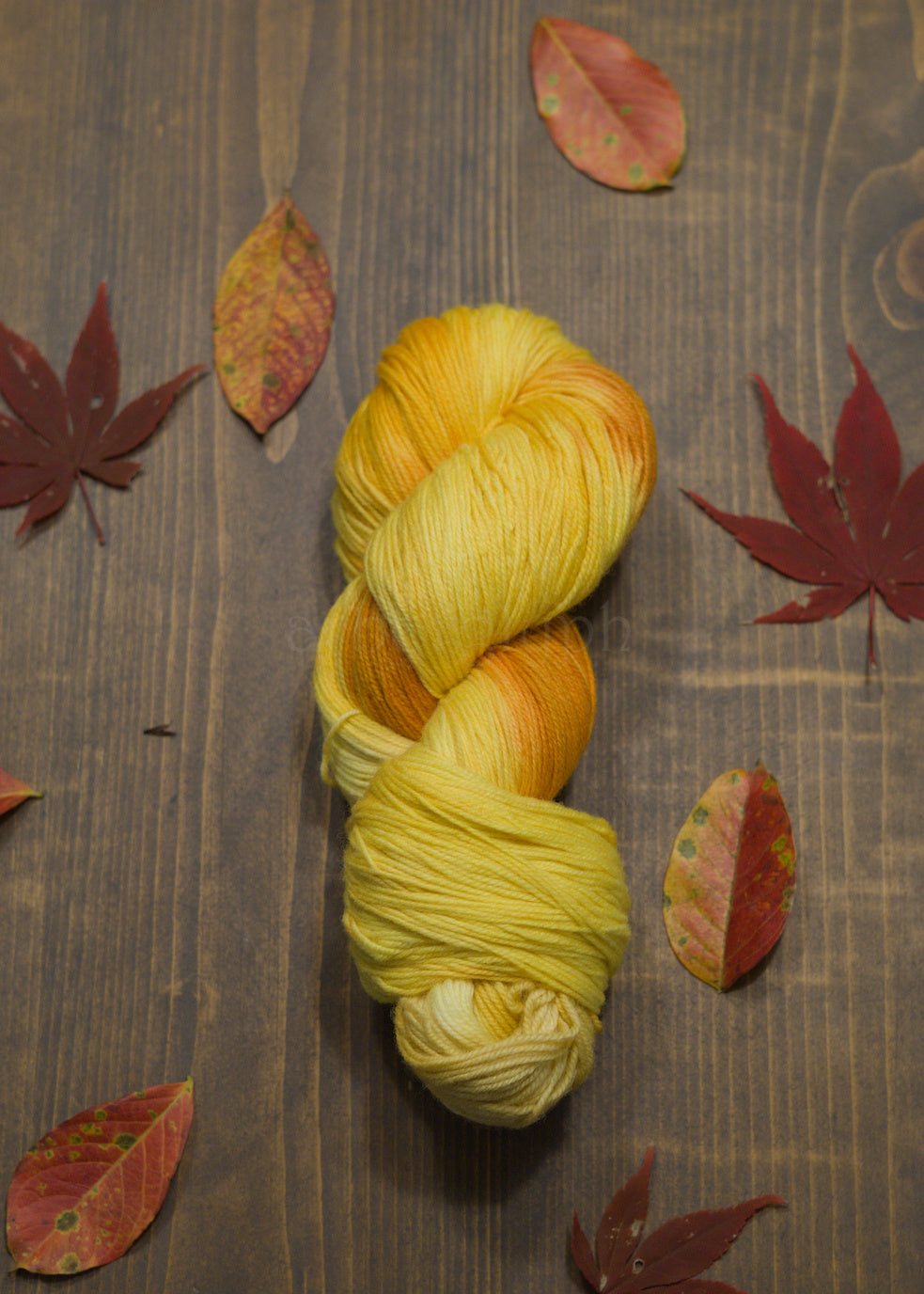 Yellow skein of yarn on a wooden surface with autumn leaves
