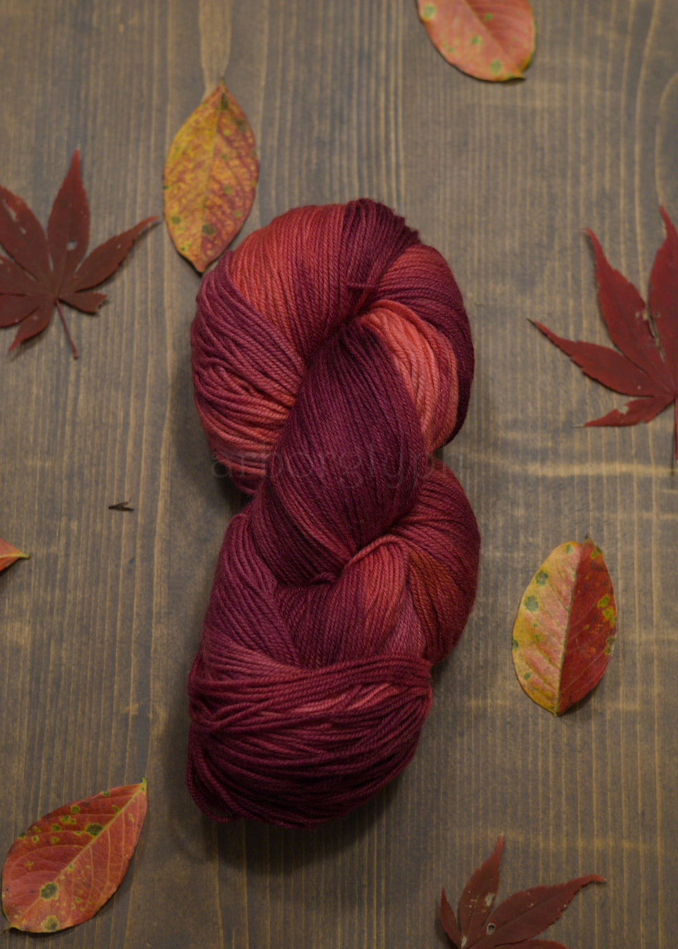 Red skein of yarn on a wooden surface with autumn leaves
