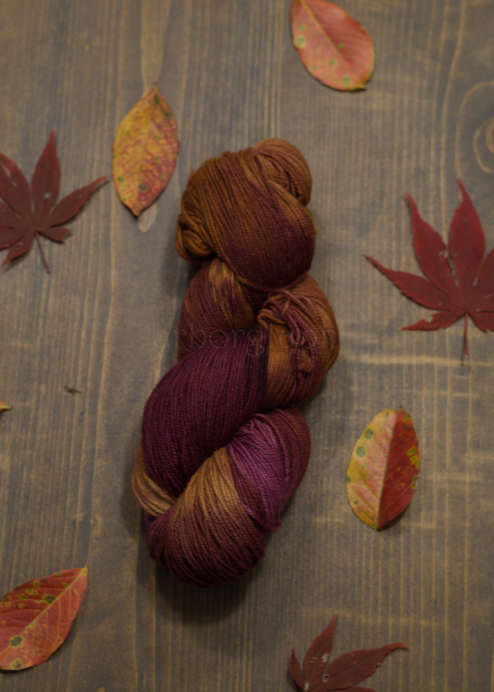 Skein of multicolored, burgundy and copper, yarn on a wooden surface with autumn leaves.
