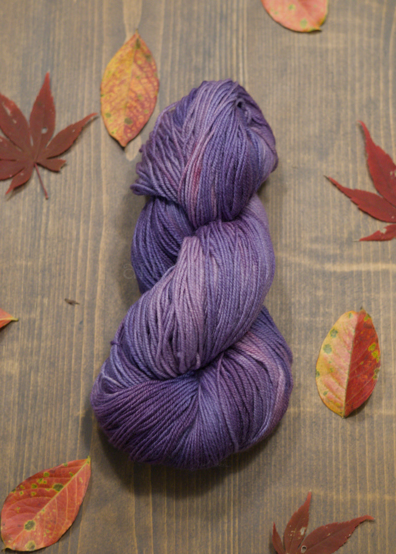 Purple skein of yarn on a wooden surface with autumn leaves