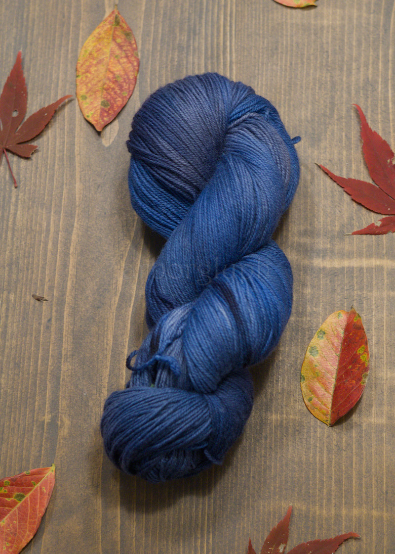 Blue skein of yarn on a wooden surface with autumn leaves