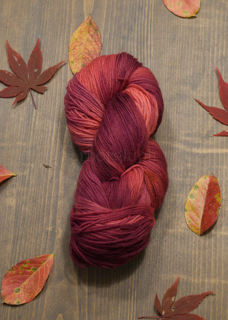 Red skein of yarn on a wooden surface with autumn leaves