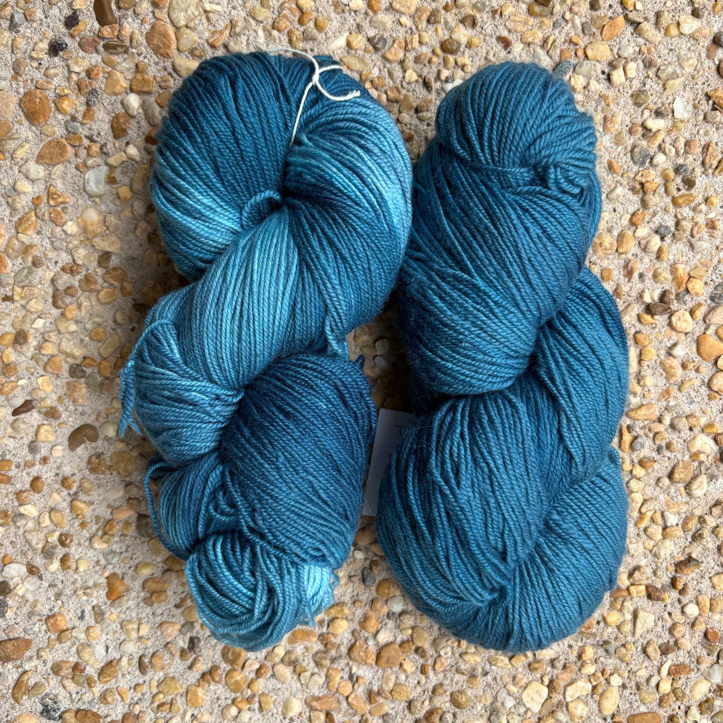 Two skeins of hand dyed blue yarn on a textured surface