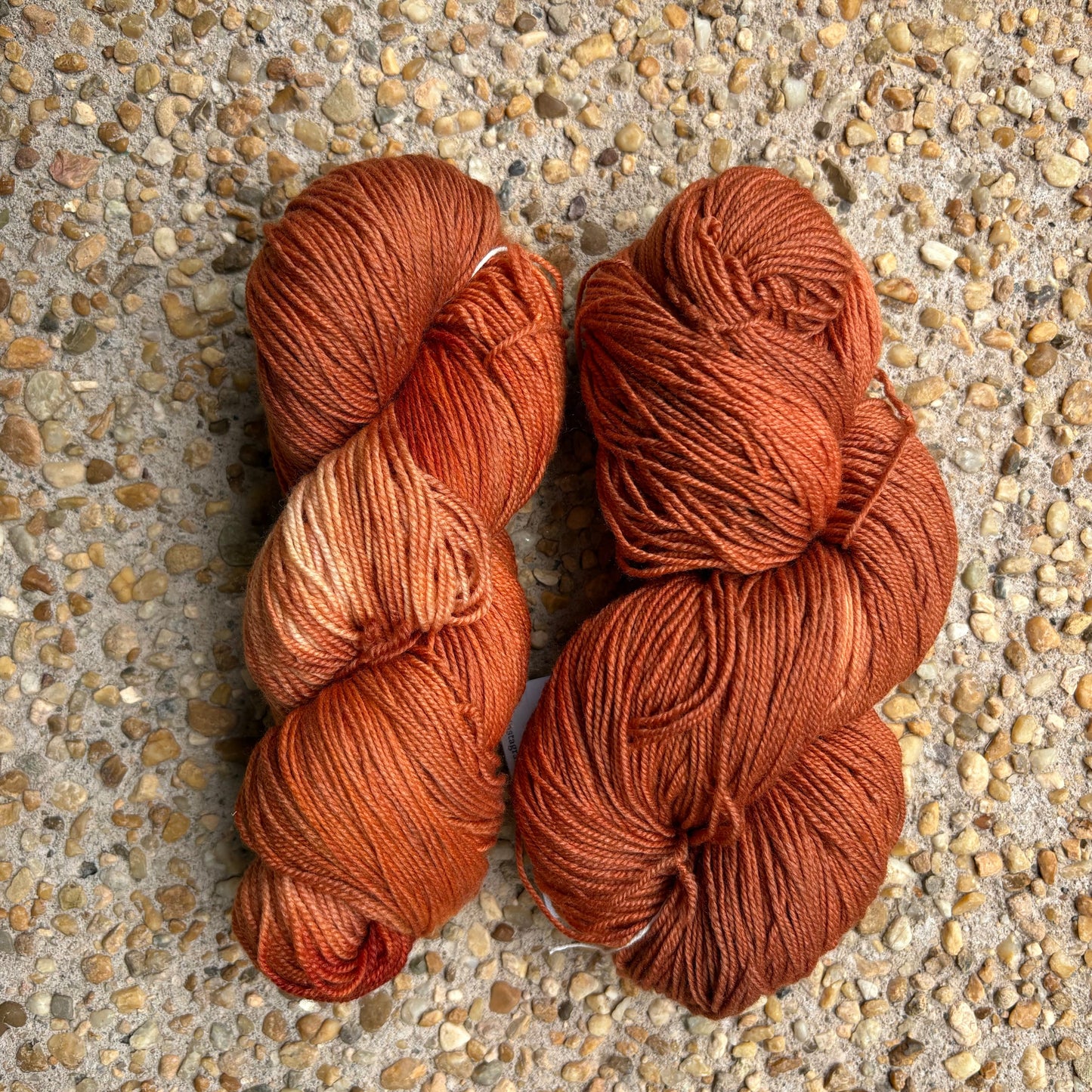 Two skeins of copper yarn on a textured surface