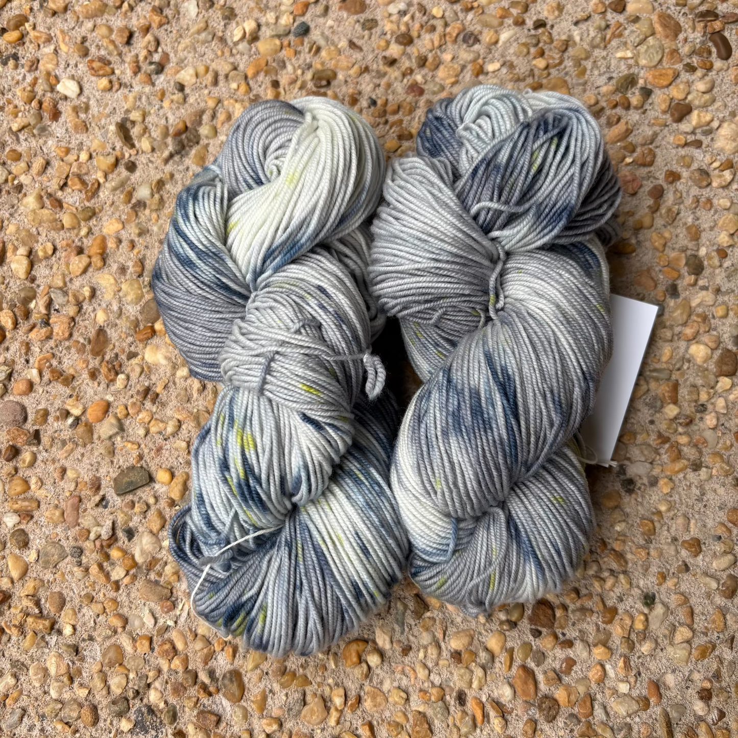 Three skeins of blue and white yarn on a pebbled surface