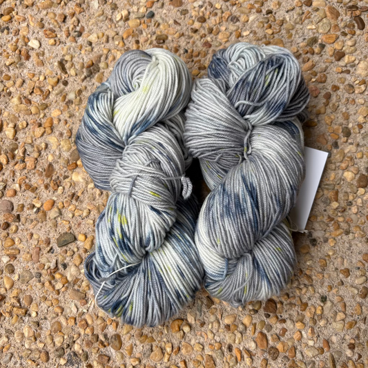 Three skeins of blue and white yarn on a pebbled surface