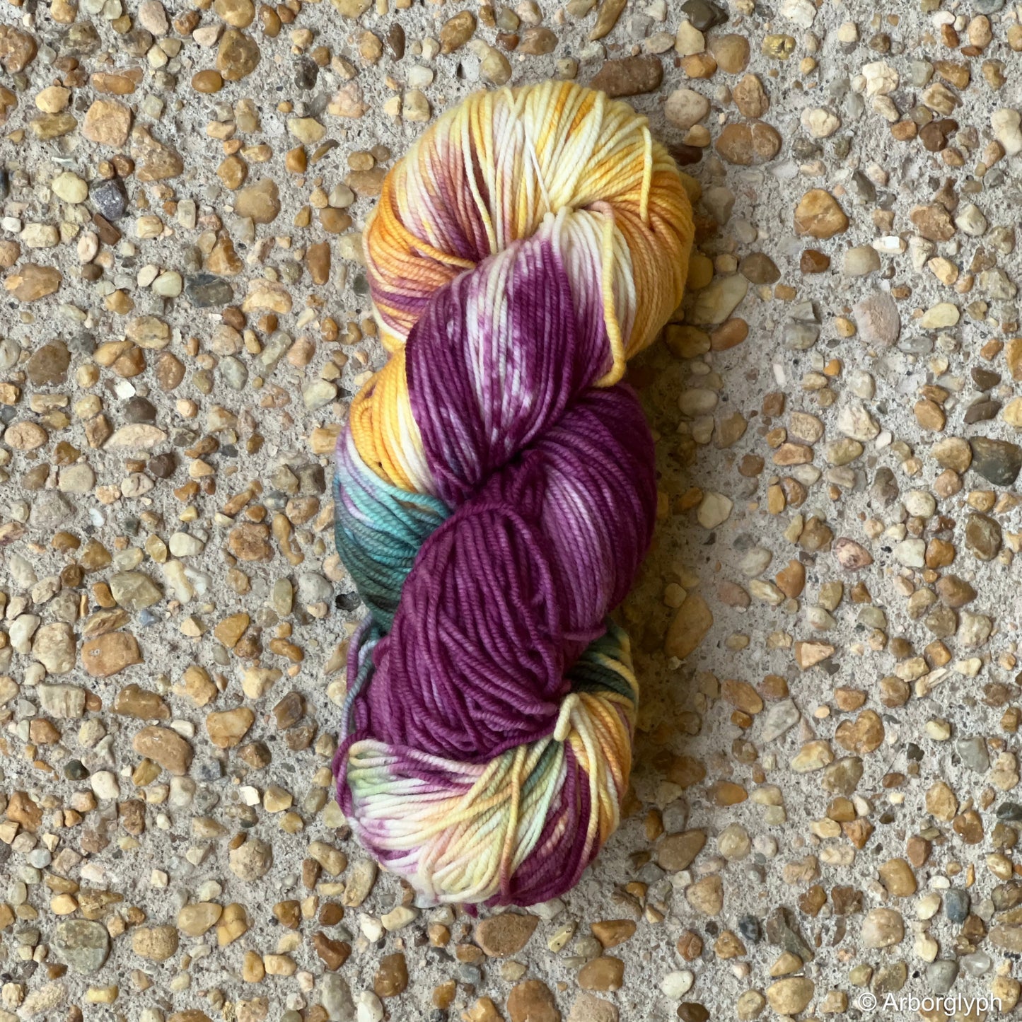 Skein of hand-dyed Renaissance Palette yarn in plum, gold, and teal Merino