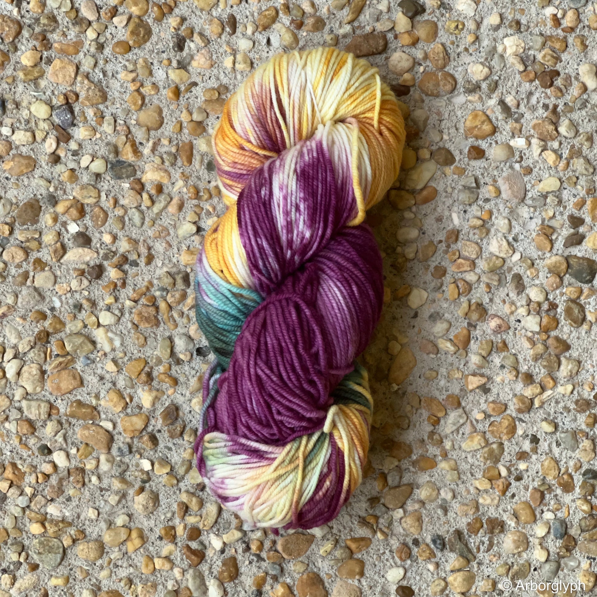 Skein of hand-dyed Renaissance Palette yarn in plum, gold, and teal Merino